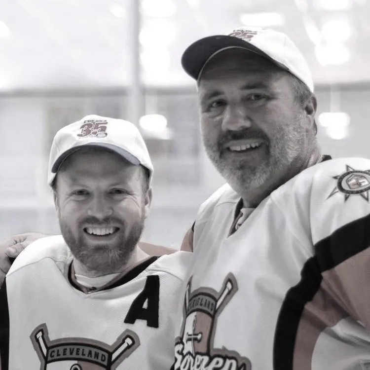 Two hockey players in team jerseys and caps, smiling, in black and white